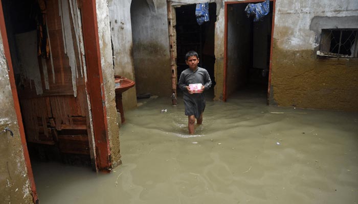 A boy wades through his flooded house after heavy monsoon rains in Karachi on Tuesday. — AFP