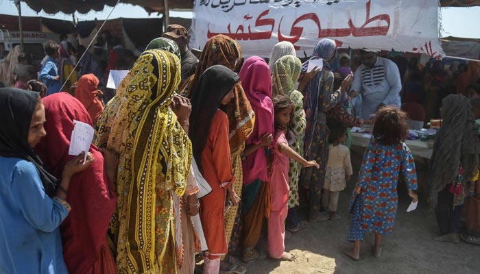 In this picture taken on September 27, 2022, internally displaced flood-affected people stand in a queue with their doctors prescriptions to get medicine at a medical camp set up for the flood affected in Jamshoro district of Sindh province. — AFP/File