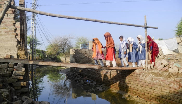 In this picture taken on October 28, 2022, students walk across a metal girder atop floodwaters in Chandan Mori, in Dadu district of Sindh province. — AFP