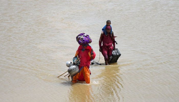 A family with their belongings wade through rain waters following rains and floods during the monsoon season in Jamshoro, on August 26, 2022. — Reuters