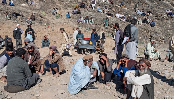 In this photo taken on November 12, 2023, Afghan refugees sit on a hilltop outside the International Organisation for Migration (IOM) office as they wait for registration upon their arrival from Pakistan near the Afghanistan-Pakistan Torkham border in Nangarhar province. — APF